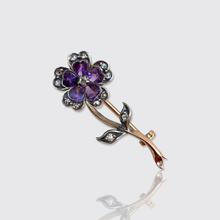 Load image into Gallery viewer, A Victorian flower brooch featuring a purple flower with silver-toned petals and a rose-gold stem with small diamonds, shown on a light gray background with a soft reflection below.