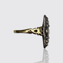 Load image into Gallery viewer, An antique ring with a gold band and a dark, textured floral face, shown from a side profile against a light gray background with a soft reflection below.